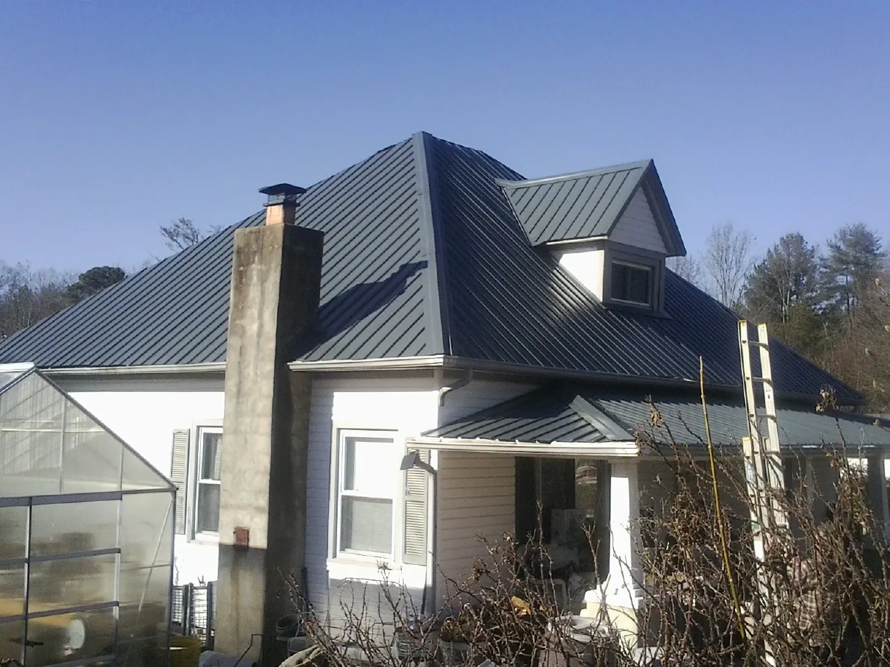 Dark blue standing seam metal roof on a white farmhouse with dormer — Slate & Tile Roof Repair by Roofing Brothers in Ordway