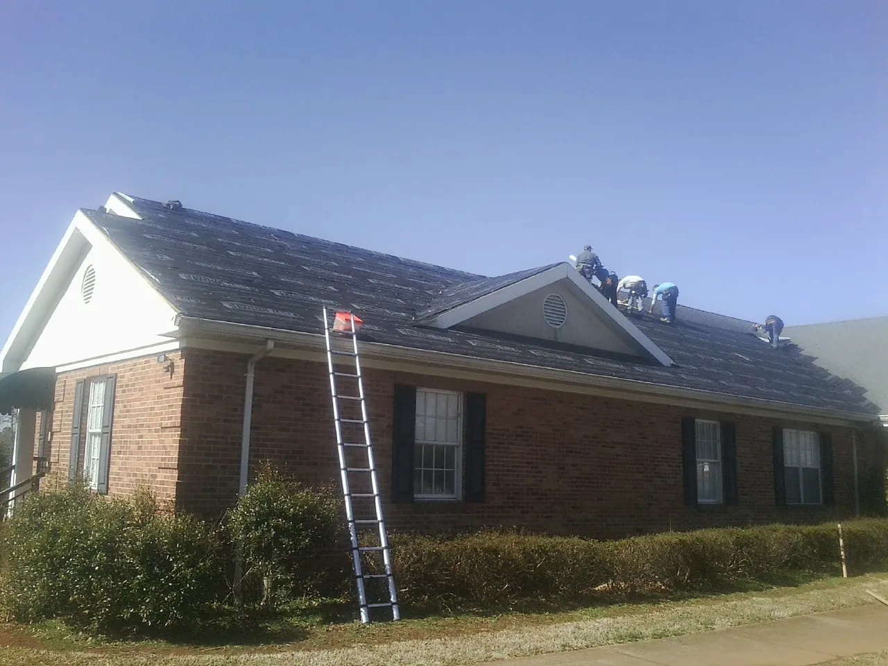 Crew tearing shingles off a brick ranch roof with a ladder set — Metal Roof Repair work by our crew in Ordway
