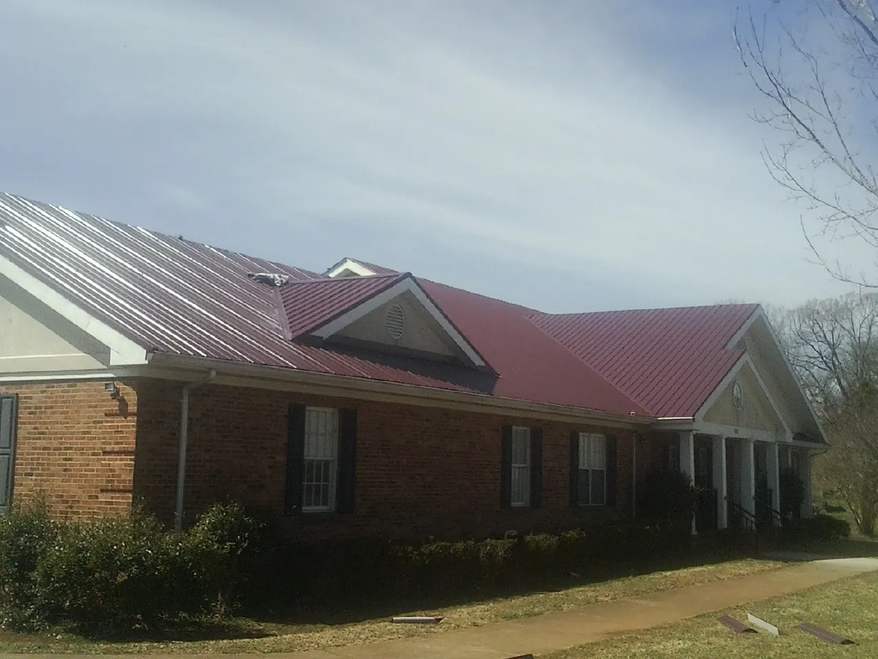 Red metal roof with gabled entries on a long brick building, from a Hail Damage Roof Repair job in Ordway