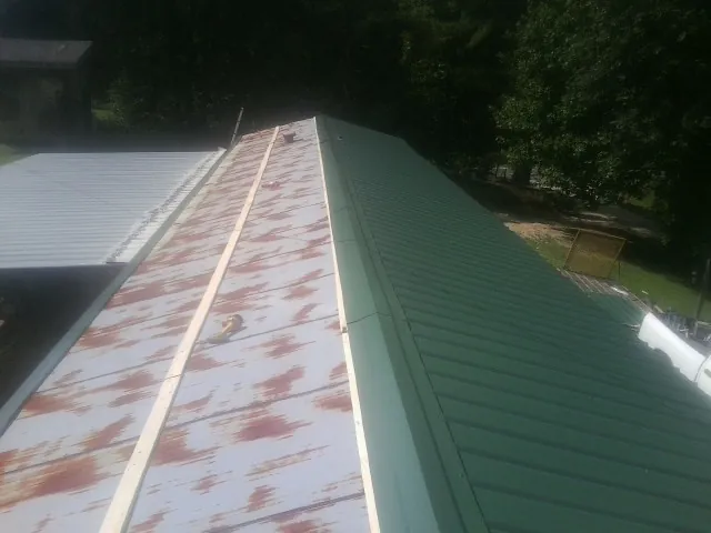 Old rusted panels beside newly installed green metal roofing — Wind Damage Roof Repair by Roofing Brothers in Ordway