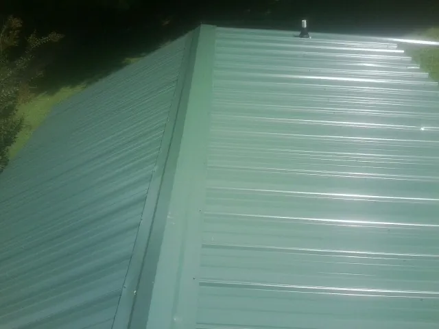 New green metal panels meeting at the ridge of a roof — Flat Roof Repair work by our crew in Ordway