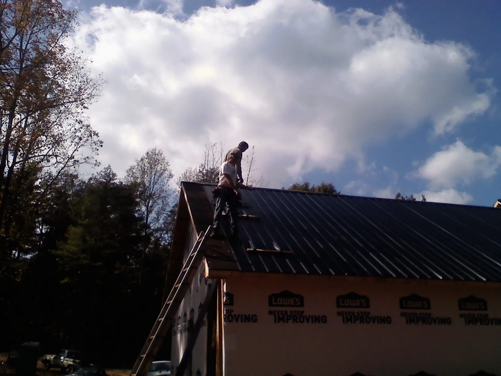 Roofer fastening dark metal panels high against a cloudy sky, from a Roof Inspection job in Ordway