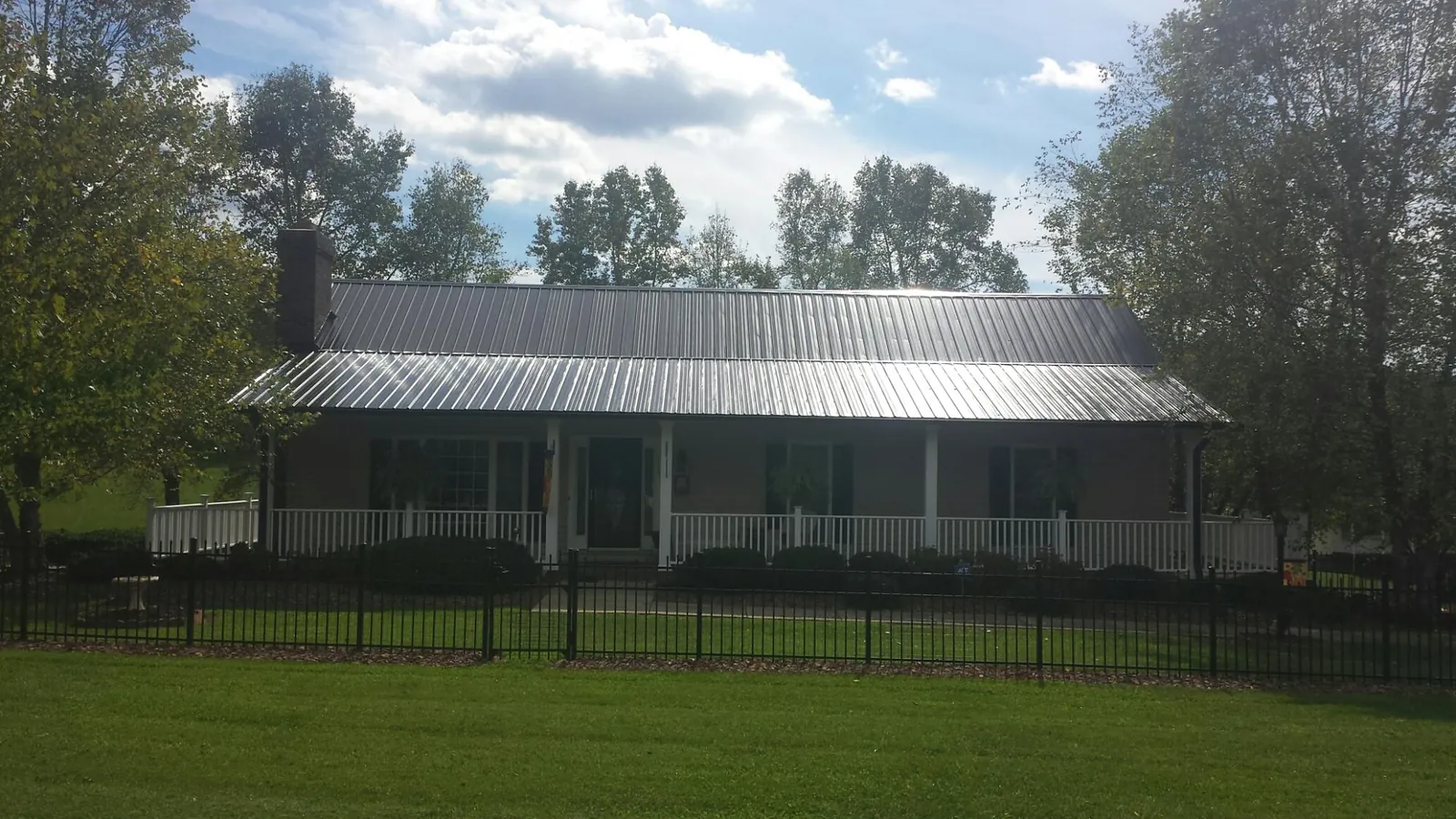 Gray metal roof on a brick ranch with a full width front porch — Gutter Guard Installation work by our crew in Ordway