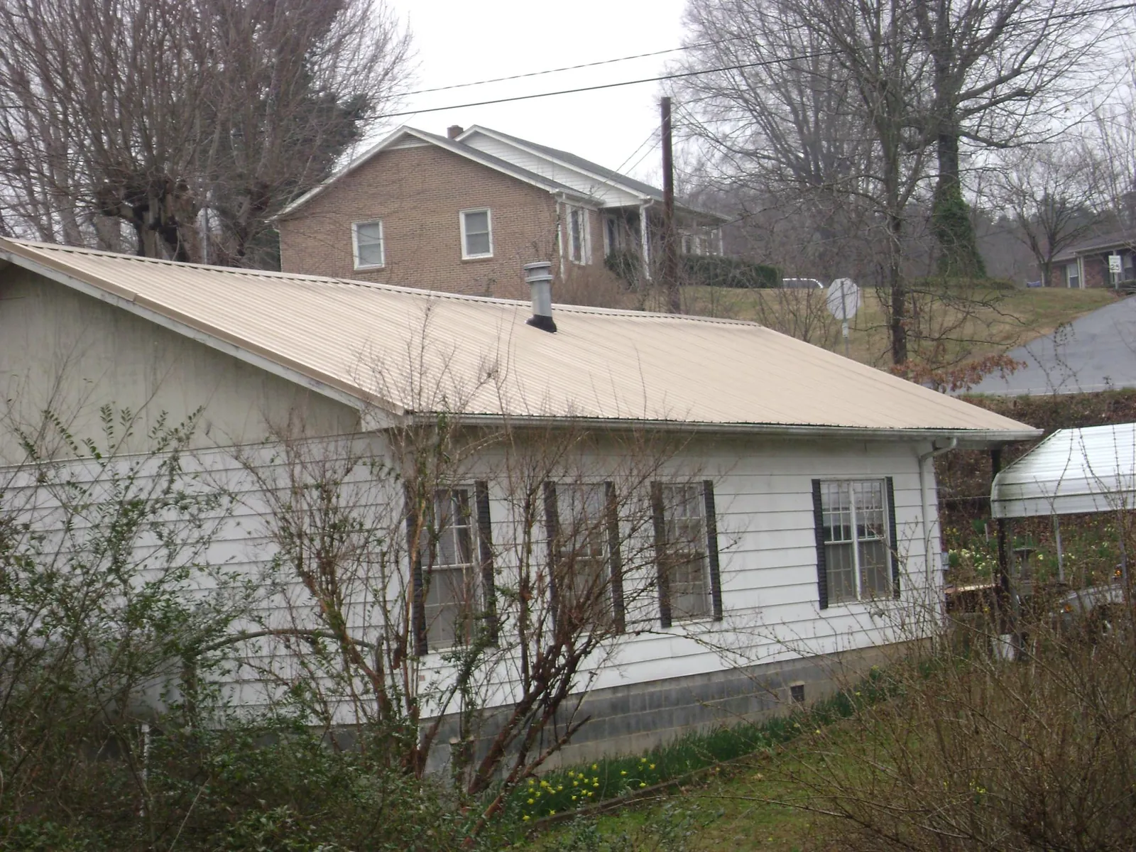 Tan metal roof on a white sided house set into a hillside — Commercial Roofing by Roofing Brothers in Ordway